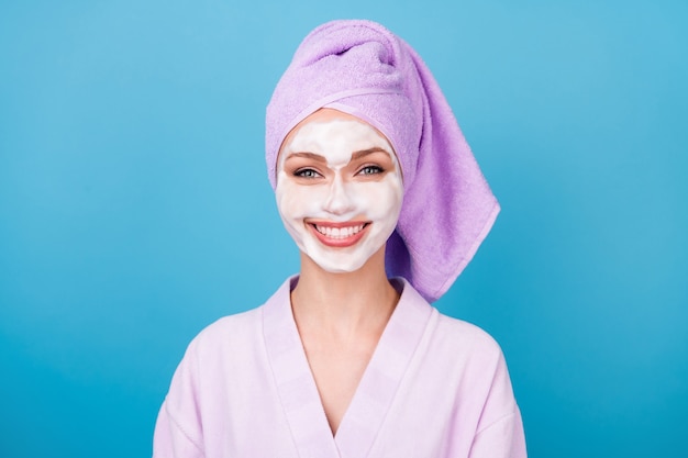 Foto de menina bonita máscara de espuma facial sorriso branco brilhante usar toalha violeta turbante roupão de banho isolado fundo de cor azul