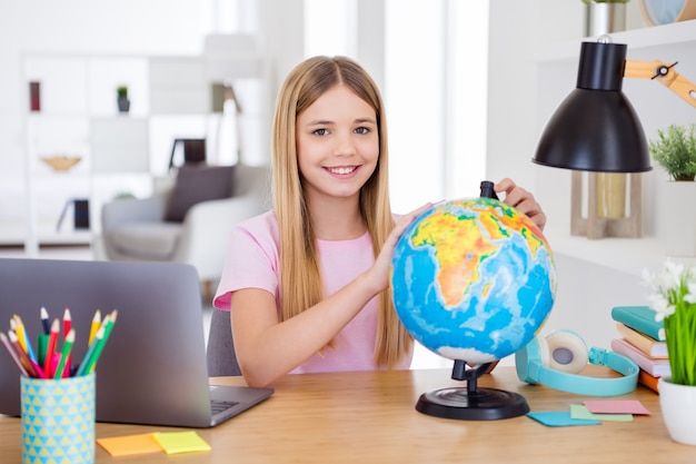 Foto de menina positiva sentada mesa mesa estudo uso remoto globo quer explorar o continente terrestre em casa dentro de casa