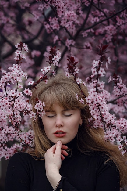 Foto de moda ao ar livre de uma linda jovem em um jardim de flor de cerejeira rosa. como uma sakura no japão.