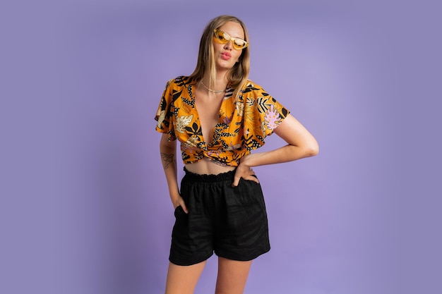 Foto foto de moda de estúdio de uma mulher loira bonita em top elegante e shorts de linho posando em fundo roxo