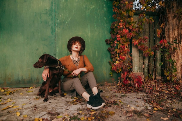 Foto de moda de senhora com cachorro no fundo da casa de campo em dia de outono