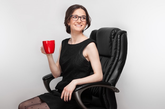 Foto de mulher bonita de vestido preto, sentado na poltrona com café nas mãos