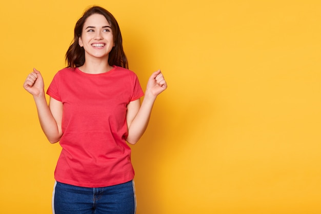 Foto de mulher bonita jovem feliz, apertando o punho enquanto sorrindo e olhando para cima isolado sobre amarelo