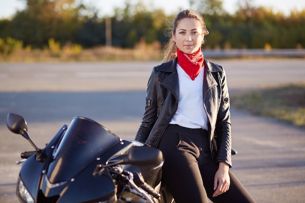 Foto de mulher bonita jovem fica perto de sua moto legal