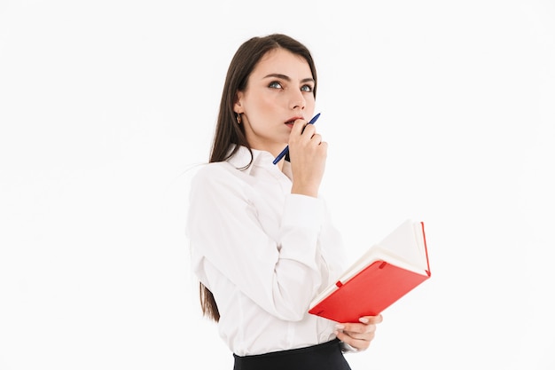 Foto de mulher caucasiana, mulher, empresária, vestida com roupa formal, segurando o planejador do dia, enquanto trabalhava no escritório, isolada sobre a parede branca