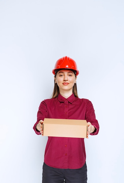 Foto de mulher com capacete vermelho segurando a caixa de papelão no fundo branco.