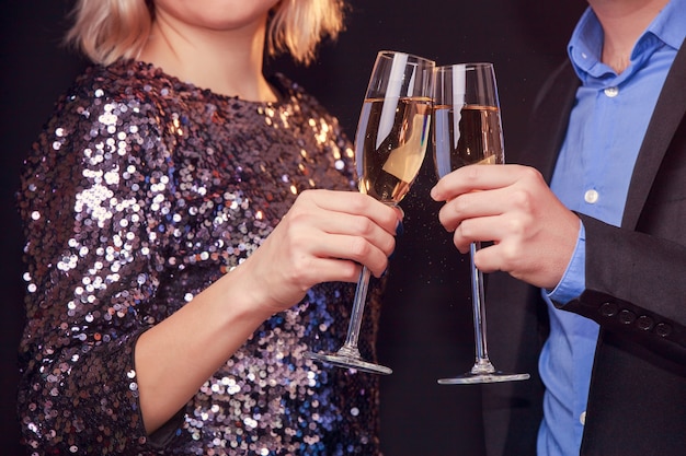 Foto de mulher com vestido brilhante e homem com taças de vinho e champanhe em fundo preto