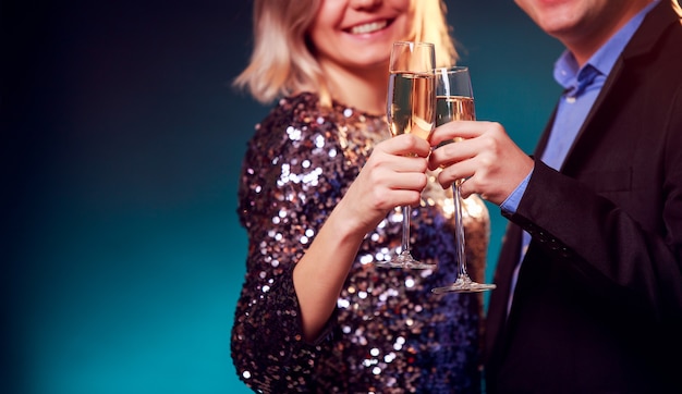 Foto de mulher com vestido brilhante e homem com taças de vinho e champanhe sobre fundo azul