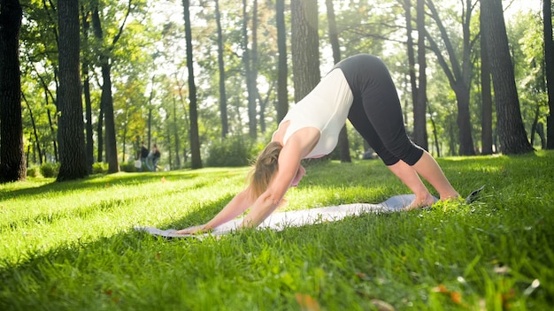 Foto de mulher de meia idade com roupas de sportrs praticando ioga ao ar livre no parque. Mulher de meia-idade alongando-se e meditando na floresta