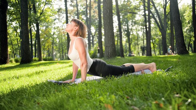 Foto de mulher de meia idade praticando ioga ou fitness na grama verde fresca no parque. Saúde física e mental feminina. Pessoa em meditação e harmonia de corpo e alma