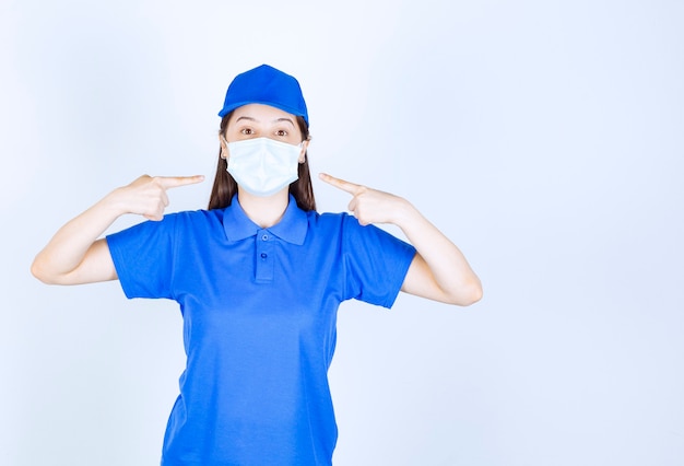 Foto de mulher de uniforme apontando para uma máscara médica.