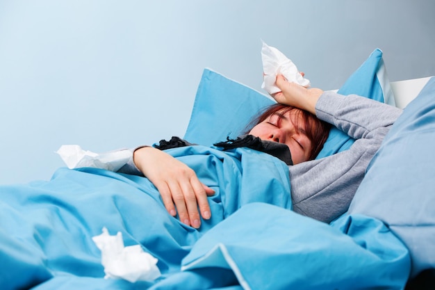 Foto de mulher doente com lenços de papel deitada na cama