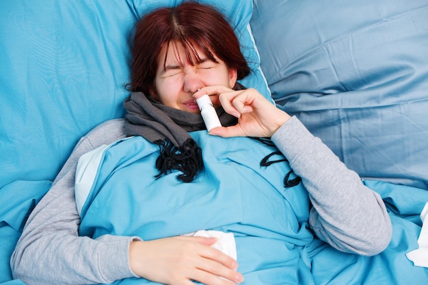 Foto de mulher doente usando spray nasal deitada na cama