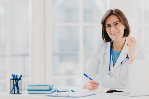 Foto de mulher estagiária trabalha no hospital, escreve em atestado médico, prescreve tratamento para paciente