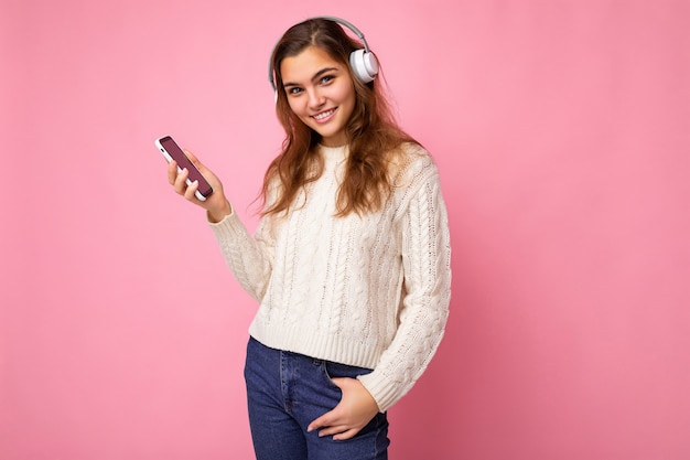 Foto de mulher jovem e bonita sexy, positiva, vestindo um suéter branco claro elegante isolado no rosa