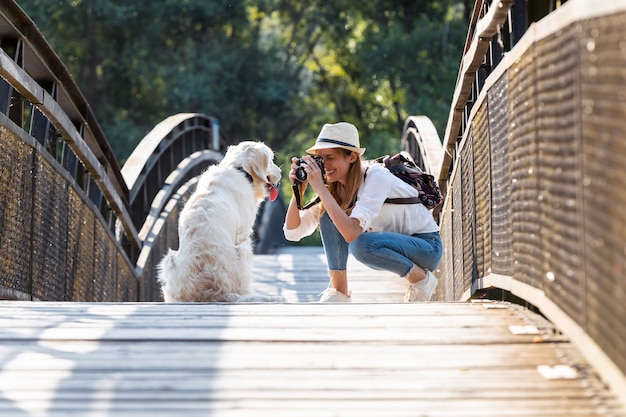 Foto de mulher jovem fotografia amador tirando uma foto de seu cachorro sentado em uma ponte no parque.