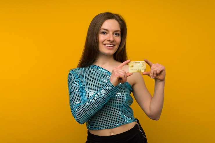 Foto foto de mulher jovem satisfeita posando isolada sobre o fundo da parede amarela, segurando um cartão de débito ou crédito.