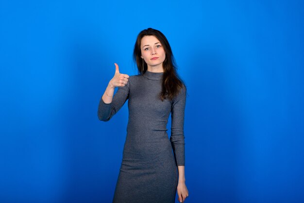 Foto de mulher jovem sorridente e alegre em um vestido cinza na parede azul. retrato emocional