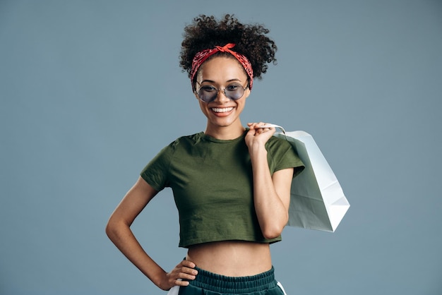 Foto de mulher modelo muito multirracial carregando pacote de cliente e sorrindo dentuço para o fundo azul da câmera isolado. Conceito de compras