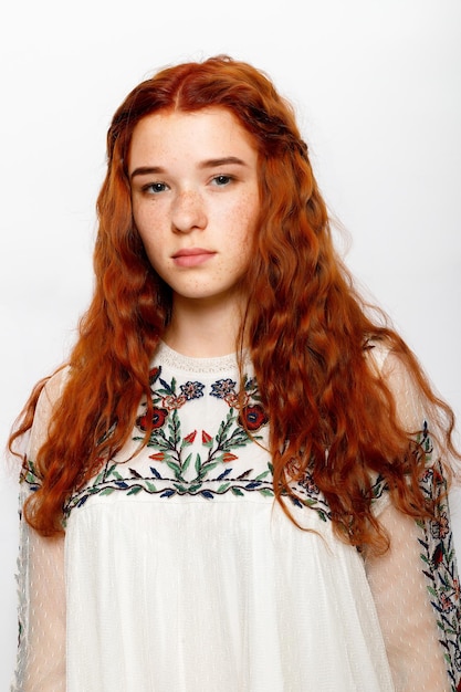 Foto de mulher ruiva bonita e séria, pele lisa e saudável tem cabelo natural ondulado vermelho vestido com jumper branco casual olha para poses de câmera no espaço de cópia de estúdio no lado direito