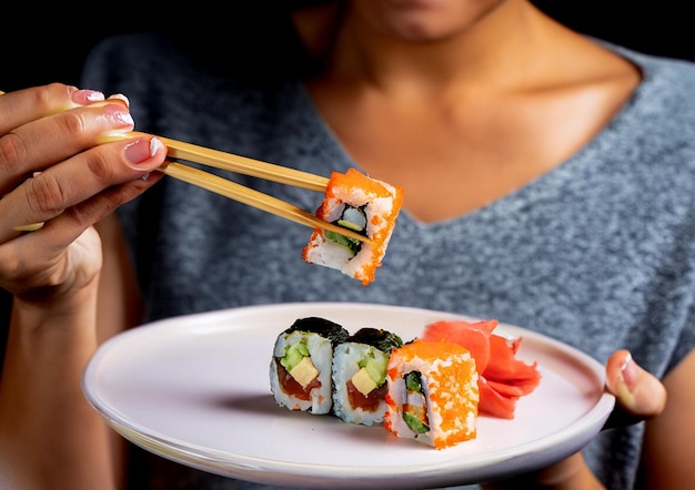 Foto de mulher segurando um rolo de sushi com pauzinhos em fundo preto