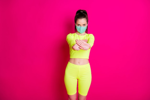 Foto de mulher usando máscara facial mostrando proibido usar roupas esportivas amarelas, isolado em um fundo de cor fúcsia vívida