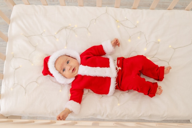 Foto de Natal de um bebê em uma roupa de Papai Noel deitado em um berço em casa, vista de cima, feliz ano novo.