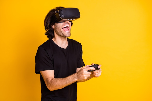 Foto de perfil de jovem realidade virtual segurar controlador boca aberta usar t-shirt com capacete vr isolado fundo de cor amarela