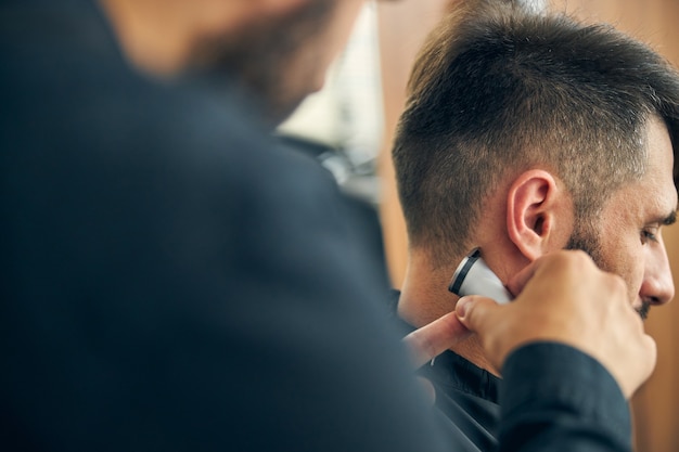 Foto de perfil de um homem moreno curvando a cabeça e ouvindo seu mestre enquanto corta o cabelo