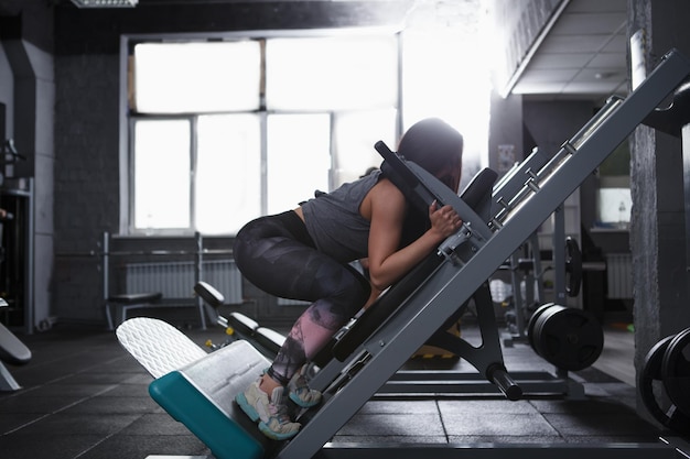 Foto de perfil de uma mulher atlética forte fazendo agachamentos na máquina de ginástica de agachamento hack