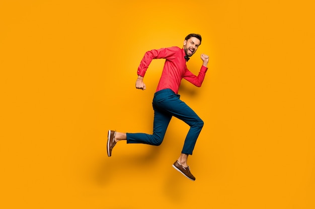 Foto de perfil em tamanho real de um cara engraçado pulando alto em um shopping center preto sexta-feira usando uma camisa vermelha na moda e calça de gravata borboleta.