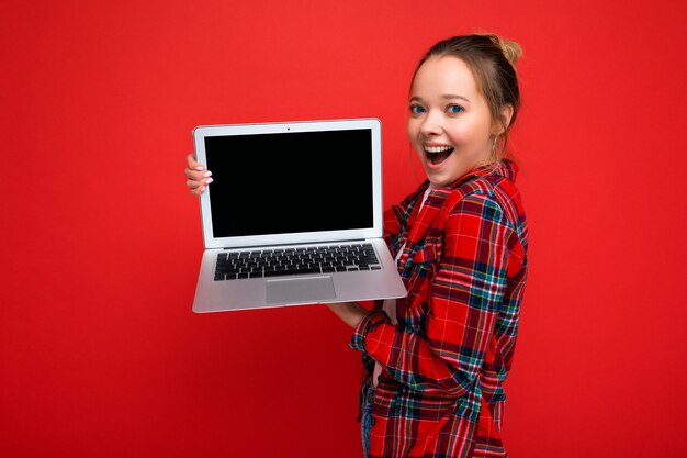 Foto de perfil lateral de uma jovem encantadora muito surpresa e surpresa segurando um laptop de camisa vermelha