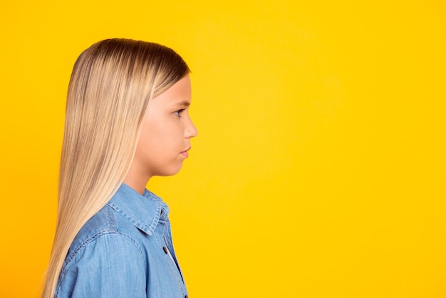 Foto de perfil lateral de uma menina muito séria e calma, vestindo uma camisa jeans, olhando para um espaço em branco, isolado em um fundo de cor amarela vívida