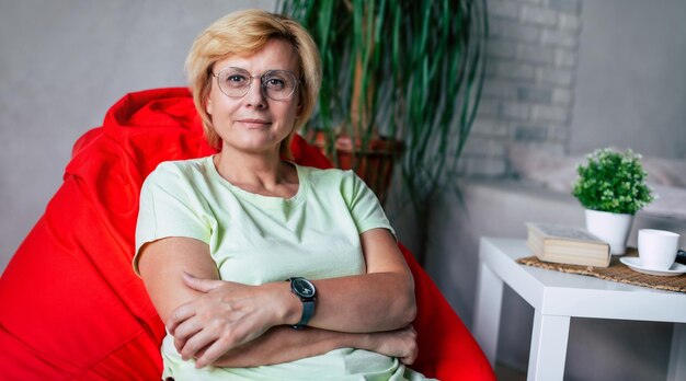 Foto de perto de uma mulher madura e feliz de meia-idade sentada em uma cadeira em casa na sala de estar relaxando Sucesso e satisfação estilo de vida aposentadoria feminina ter descanso atividade de lazer