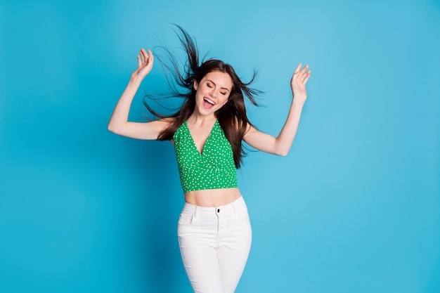 Foto de positiva encantadora menina bonita desfrutar dança vento sopro corte de cabelo levantar mãos usar camiseta isolada sobre fundo de cor azul