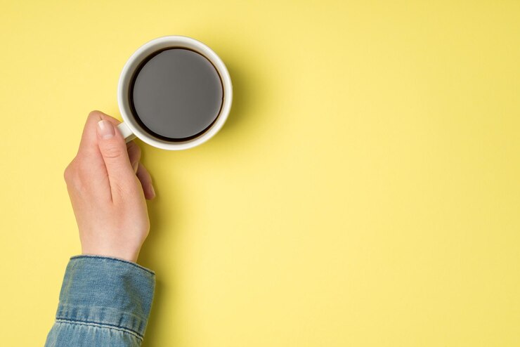 Foto foto de primeira pessoa da vista superior da mão feminina segurando uma xícara branca de café em fundo amarelo isolado com espaço para cópia