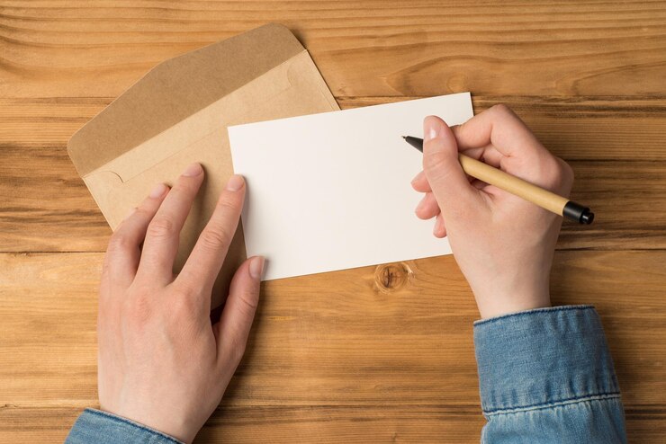 Foto foto de primeira pessoa vista superior de mãos segurando uma caneta sobre cartão branco e envelope de papel ofício em fundo de mesa de madeira isolado com espaço em branco