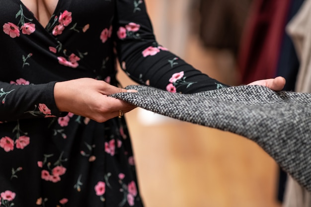 Foto de qualidade do tecido de um suéter cinza, cuidadosamente examinado por uma jovem.