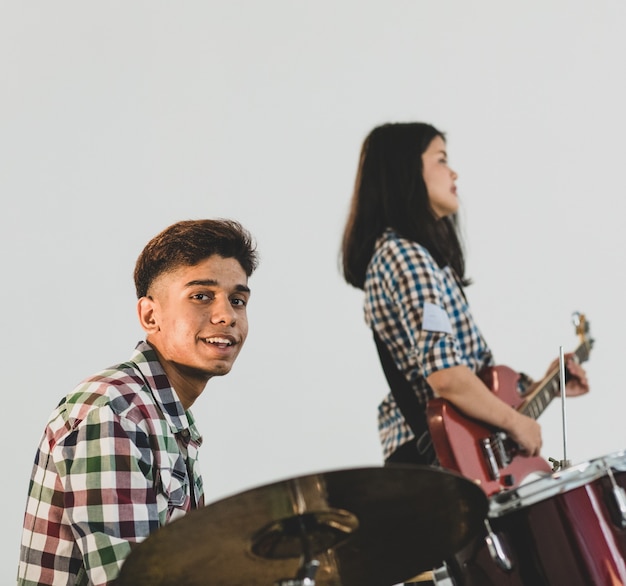 Foto foto de retrato de um baterista adolescente tocando a música. jovem músico tocando bateria com um guitarrista ao fundo. estudante profissional júnior tocando um instrumento como hobby com amigos