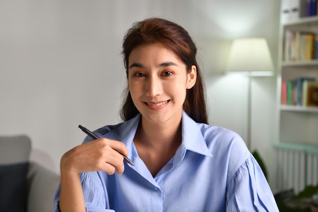 Foto de retrato de uma empresária asiática feliz, amigável e confiante, fazendo videochamada, olhando para a câmera e conversando, discutindo estratégia com parceiros on-line em casa