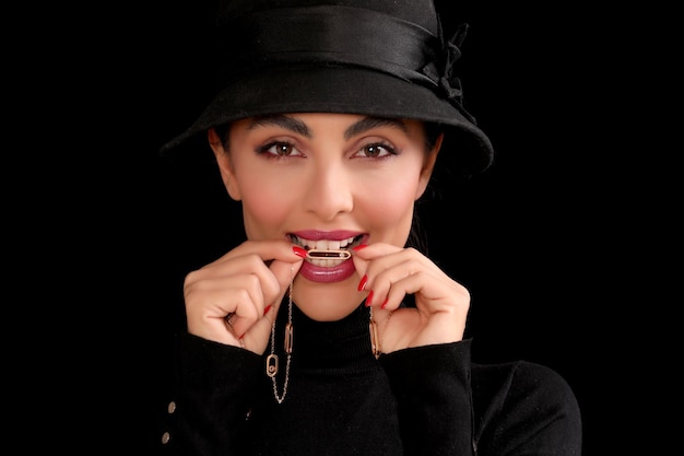 Foto de retrato de uma garota clássica com um colar entre os dentes e chapéu preto