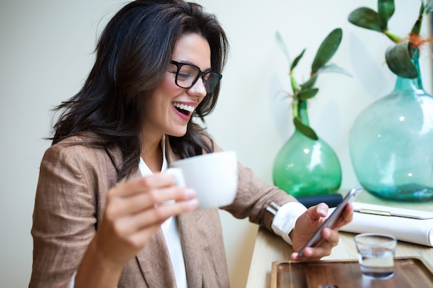 Foto de rindo de mensagens de texto de jovem empresária com seu telefone celular no café.