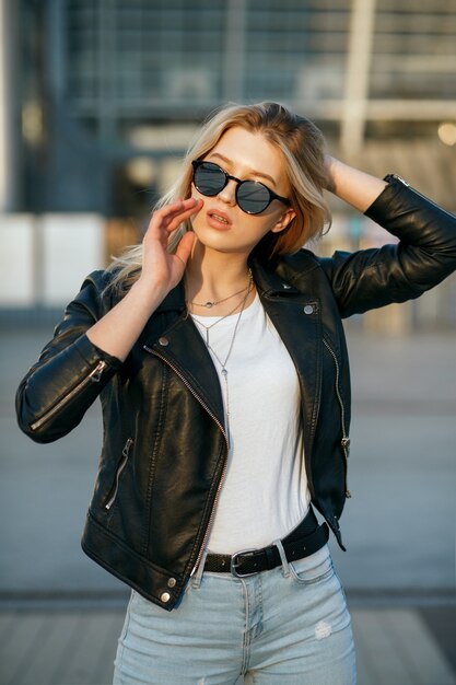 Foto de rua de uma jovem elegante usando óculos escuros e jaqueta preta