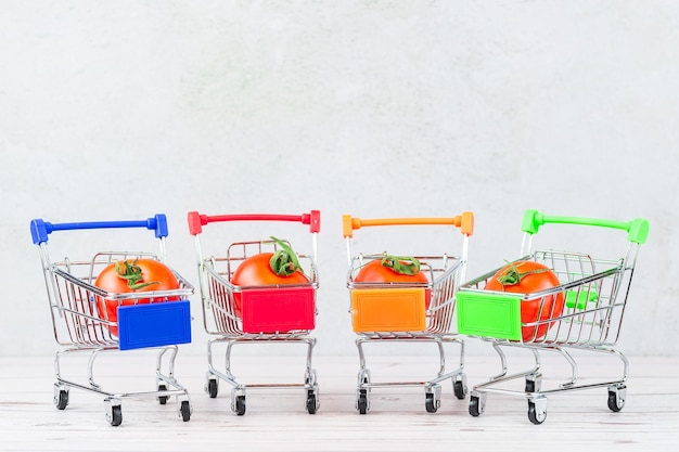 Foto de saborosos tomates maduros no carrinho de compras ou carrinho na superfície branca