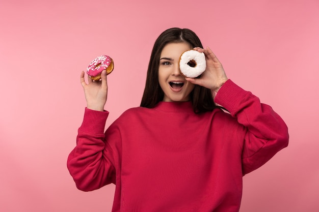 Foto de senhora atraente detém olhos cobertos doces donut doces alimentos desgaste sorriso feliz camisola rosa casual isolado fundo de cor rosa.