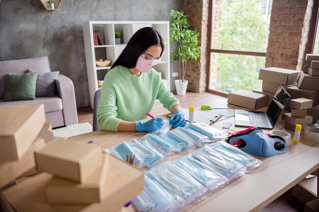 Foto de senhora chinesa asiática com luvas de látex negócios organizar pedido rosto máscaras médicas pacote feito à mão colocar escrever endereço do cliente cartão de papel loja online entrega escritório doméstico dentro de casa