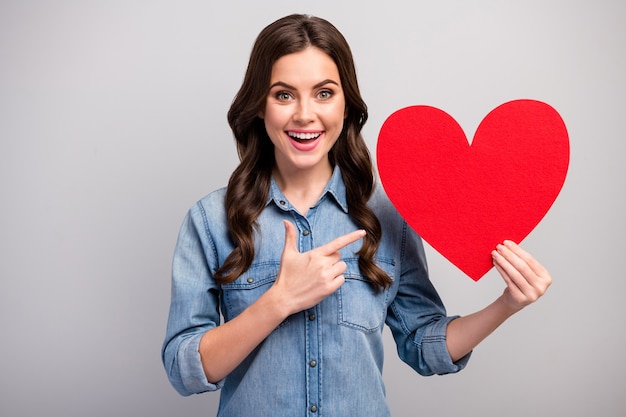 Foto de senhora muito engraçada indica dedo grande coração de papel vermelho comemorando o dia dos amantes convite legal ideia incomum usar jeans casual camisa jeans isolada cor cinza