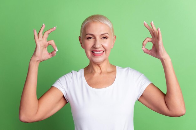 Foto de senhora sênior de bom humor mostra os dedos okey símbolo anúncio grande isolado sobre o fundo de cor verde.