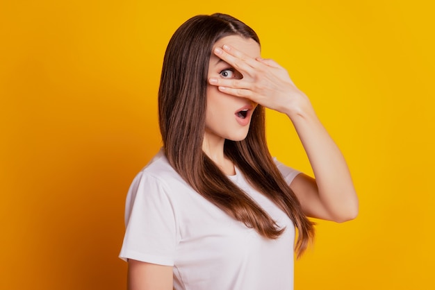 Foto de senhora tímida capa de mão olhos espreita usar camiseta branca posando em fundo amarelo