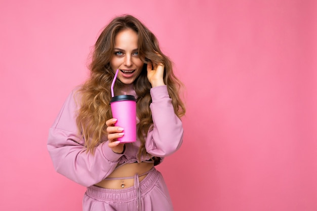 Foto de sexy atraente jovem feliz sorridente mulher loira vestindo roupas elegantes todos os dias, isolada sobre a parede de fundo colorido, segurando o copo de papel para recorte bebendo chá olhando para a câmera. espaço livre